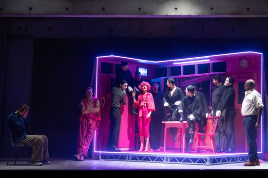 A bright pink kitchen with a neon pink light surrounding the edge. There are multiple people, most in black, and one in bright pink.