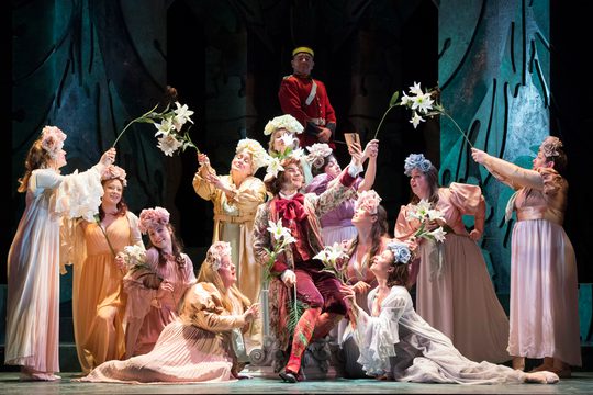 A group of women in pastel dresses and flowery headdresses. Some of them are also holding flowers.