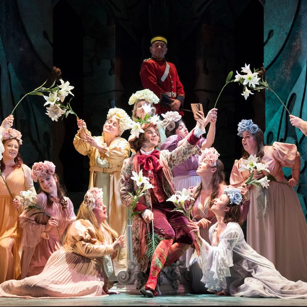 A group of women in pastel dresses and flowery headdresses. Some of them are also holding flowers.