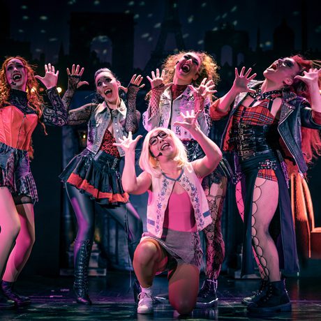 A group of women singing in a diner with their hands by their faces.