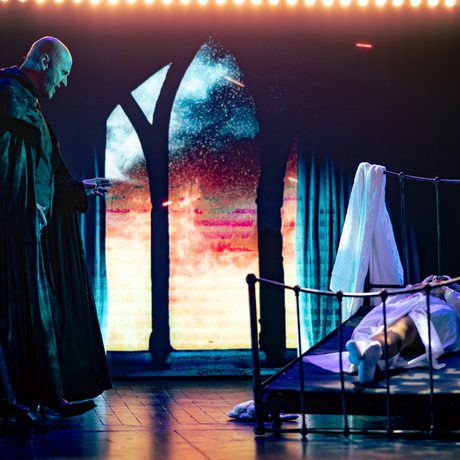 A woman lay in bed with a vampire standing over her.