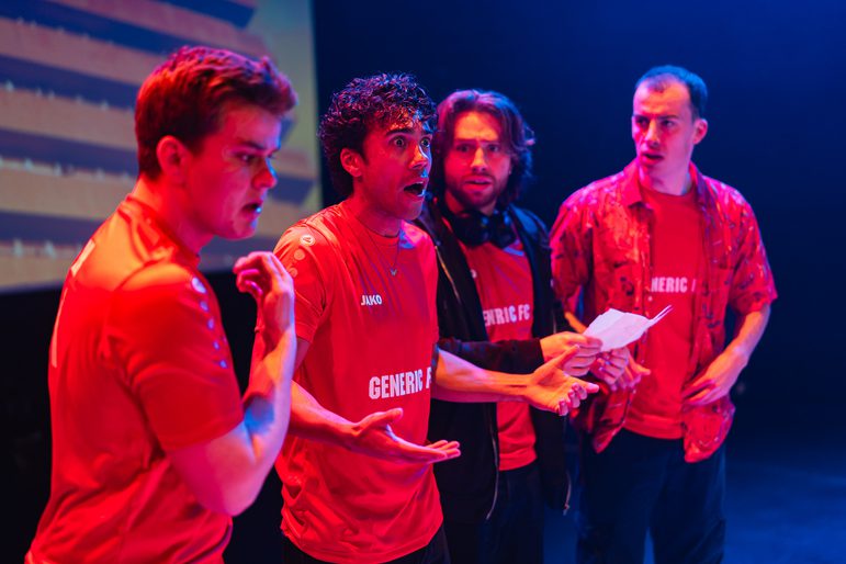 Four men in red football shirts look surprised while reading a note on paper.