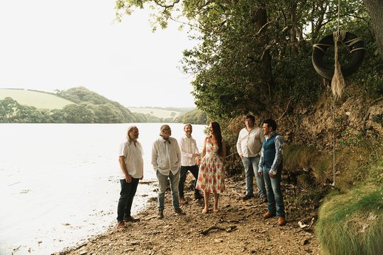 Members of the band standing by a lake.