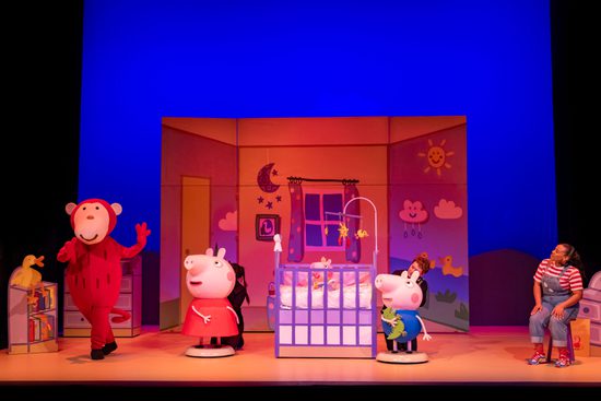 Peppa Pig and George are in a bedroom with a cot, watching a red monkey dance.