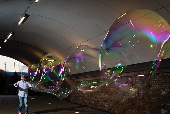 A man in a white shirt and blue jeans creates a large bubble in a tunnel.