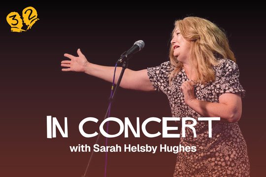 A blonde woman singing at a microphone. She has one arm stretched out in front of her.