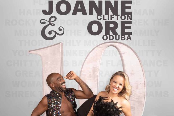 A black man in a sparkly jacket and a white, blonde woman in a black dress with feathers. They are laughing.