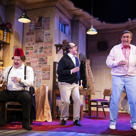 Tommy Cooper, Eric Morecambe, and Bob Monkhouse standing in a dressing room and laughing together.
