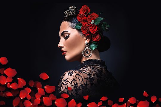 A lady in a black top with red flowers in her hair, surrounded by red petals.