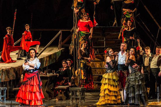 A large group of people in vibrantly coloured costumes standing on and around a set of stairs.