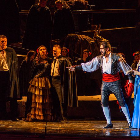 A man next to a lady in a blue dress, pointing at a crowd of people.