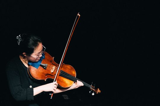 A woman dressed in black playing the viola. The background is black.