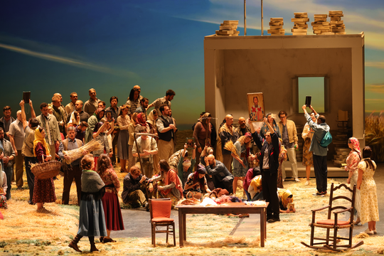 A large group of people congregating. They are holding produce and farming equipment.