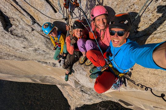 A man, a woman, and two children in colourful clothes, wearing helmets and hanging from ropes on a cliff face.