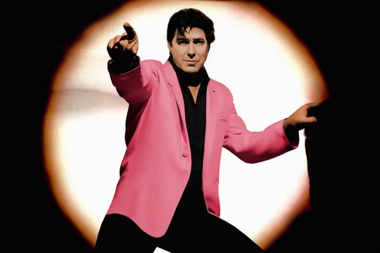 A man in a pink jacket pointing forwards.