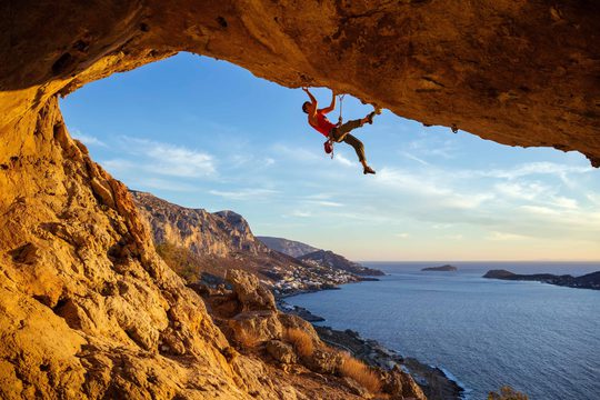 Someone climbing on a large cliff face. The sea is in the background.