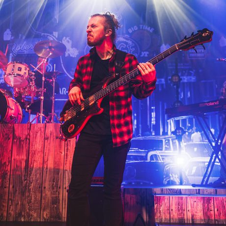 man in a red and black checked shirt plays bass guitar