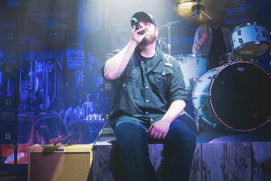 Performers sit on the edge of the stage singing out to audience