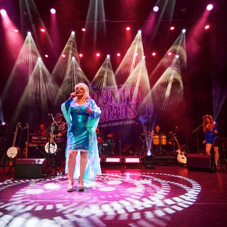 Performer dressed as Dolly Parton sings in centre stage