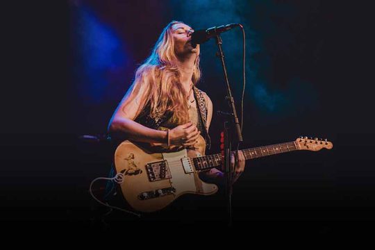 A woman with blonde hair playing the electric guitar.