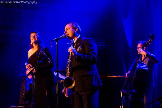 Man singing into microphone while holding a saxophone