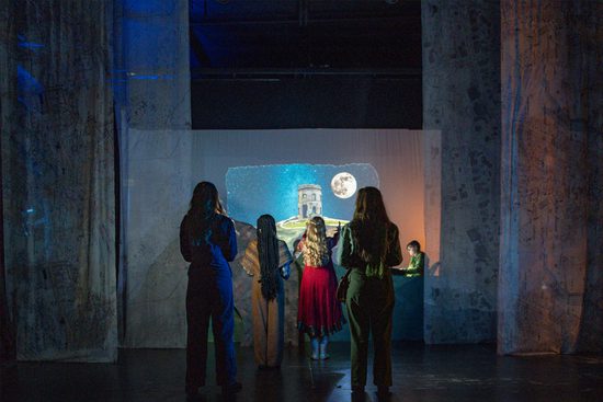 Four women facing away from the camera. They are looking at a screen with a castle on a hill projected onto it.