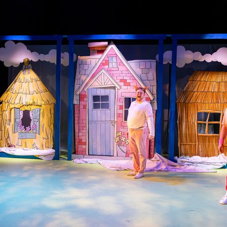 The Three Little Pigs are standing in front of three houses. One is made of straw, one of wood, and one of bricks.