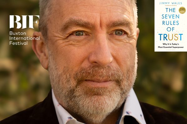 White man with grey hair and beard smiles. Trees are visible in the background.