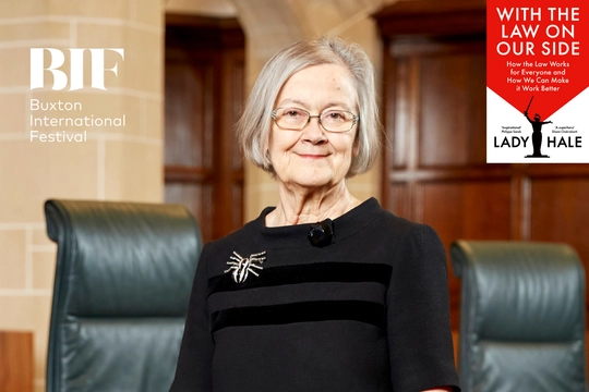 Woman with a grey bob smiles to the camera. She wears a brooch shaped like a spider.