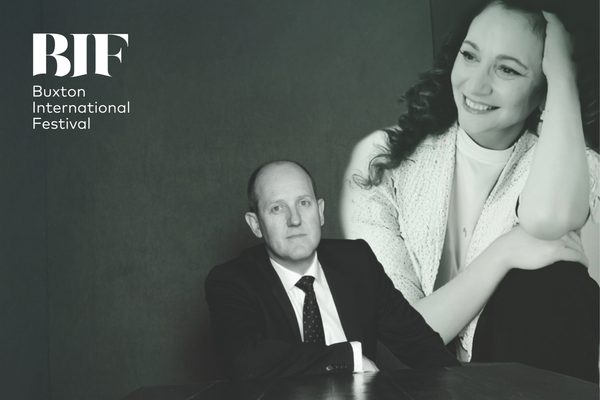 Woman with brunette curly hair smiles resting her elbow on her knee. She wears a pale shirt and jacket. Beside and image of a man smiling into the camera wearing a suit and tie.