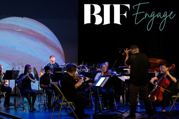 An orchestra wearing all black playing on a stage.