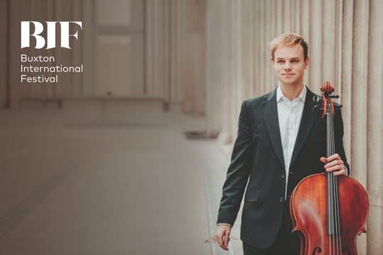 Bond man in white shirt and suit jacket, smiles while holding a cello.