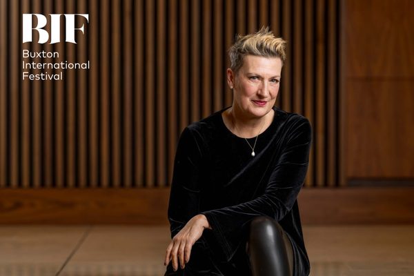 White woman with short blonde hair and red lipstick smiles to the camera. She is wearing a black velvet dress.