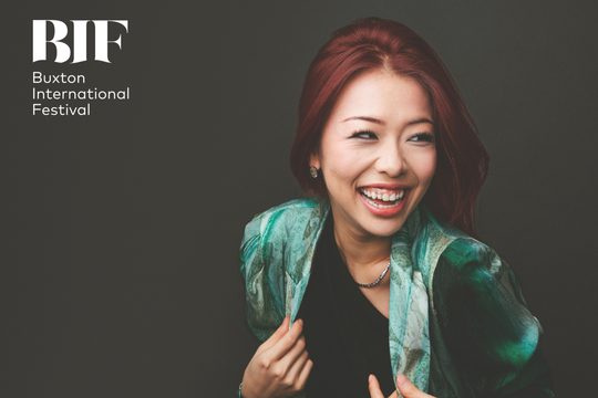 Woman with red hair laughs. She is wearing a pattered turquoise jacket.