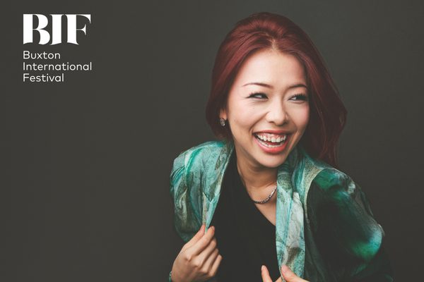 Woman with red hair laughs. She is wearing a pattered turquoise jacket.