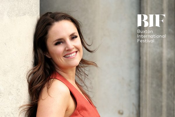 White woman with brunette hair smiles at camera wearing a pink dress.