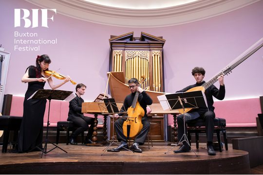 Four people play various string instruments in from of a large organ.