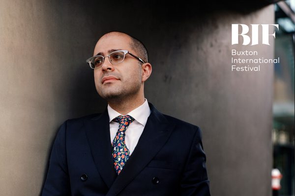Man with short shaved hair and silver rimmed glasses wears a suit with a brightly coloured flowery tie.