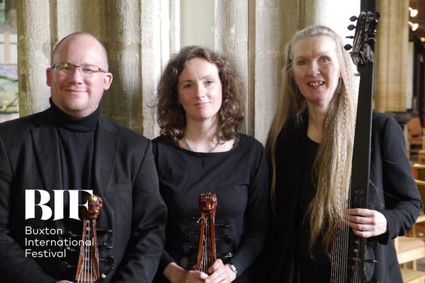 Three people a bald man with glasses, a brunette woman with curly hair and a blonde woman with long straight hair smile to the camera. The wear all black.