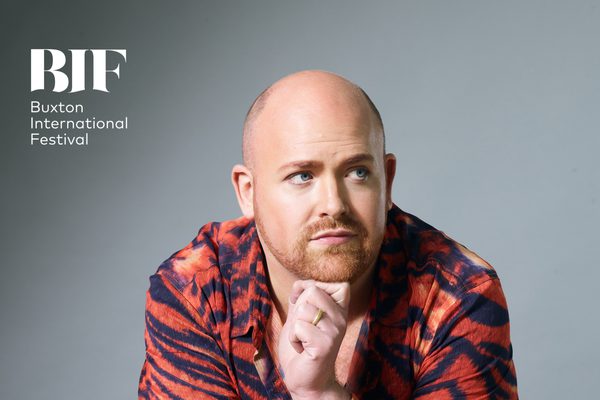 Bald man with ginger stubble clasped his hands underneath his chin and looks to the side.