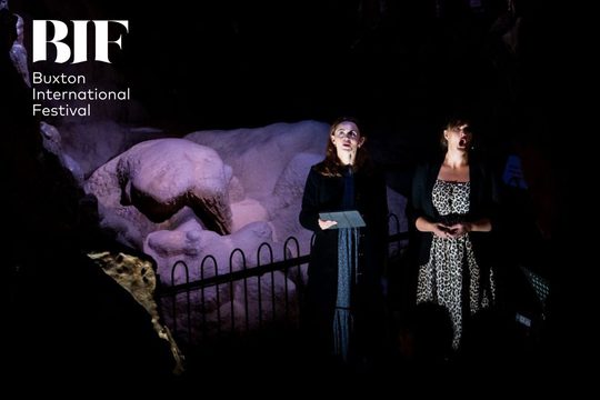 Two women sing in a dimly lit cave.