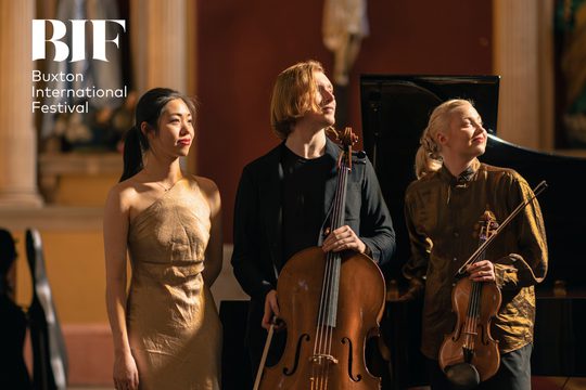 Three musicians musicians wearing black and gold look off smiling to the side.