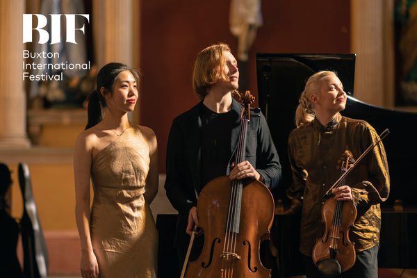 Three musicians musicians wearing black and gold look off smiling to the side.