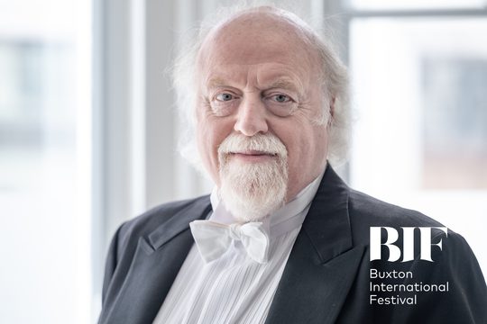 Man with white hair and beard smiles to the camera wearing white tie.
