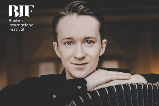 White man with pale hair and blue eyes rests his head on his arms, while looking into the camera.