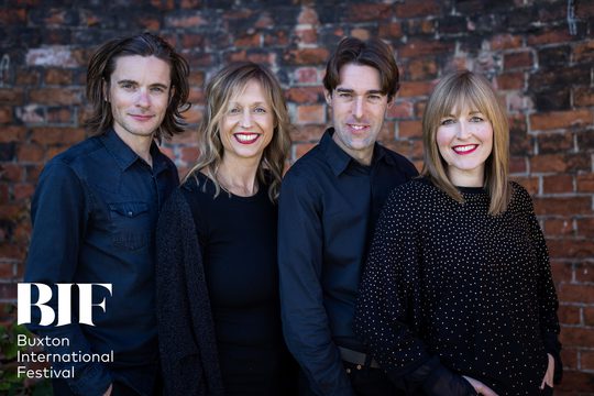 Four musicians, two women and two men smile to the camera dressed in dark casual clothes
