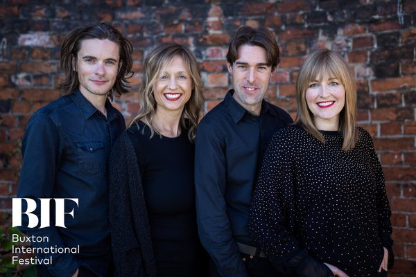 Four musicians, two women and two men smile to the camera dressed in dark casual clothes