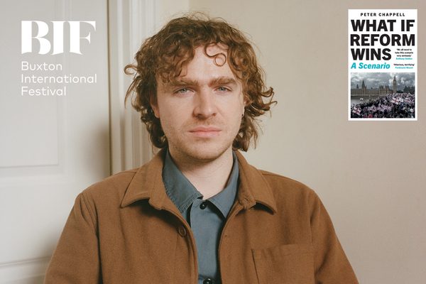 A man with curly ginger hair wearing a brown jacket and dark grey shirt.
