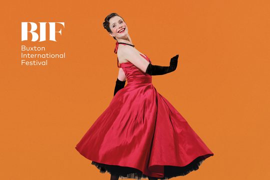 A woman in a red dress and black gloves. She is dancing and smiling.