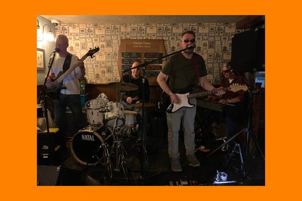A band playing in a pub. There are two guitars, drums, and a keyboard.